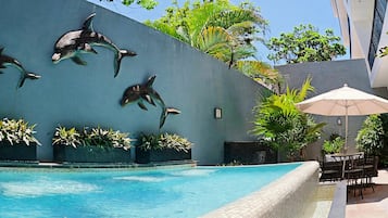 A swimming pool with dolphin sculptures on the wall, surrounded by potted plants and outdoor furniture.