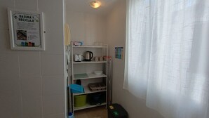 A narrow hallway with a kitchen area, including a shelf with kitchenware and a trash bin. - La Alboreá (Jerez de la Frontera)
