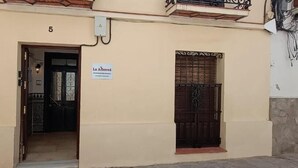 A building entrance with a door, a window with a metal gate, and a sign above the door. - La Alboreá (Jerez de la Frontera)