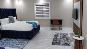 Quarto moderno com cama, escrivaninha, cadeira, televisão e dois tapetes.