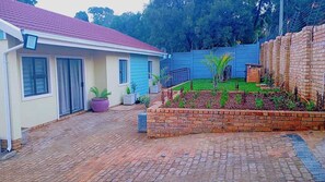 A residential property with a paved driveway, a brick garden bed, and a blue house. - The Gulf of Guinea Guesthouse  (Johannesburg)