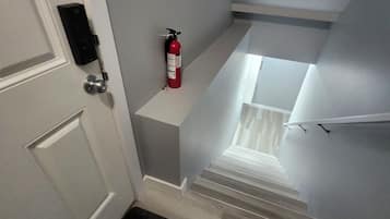 Eine Treppe mit an der Wand befestigtem Feuerlöscher, eine Tür mit Tastaturschloss und eine schwarze Fußmatte am Fuß.