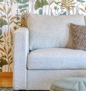 Een bank met een luipaardprint kussen tegen een muur met botanische behang.