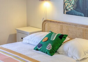 A neatly made bed with a white comforter and a green pillow with patches, a white pillow, and a wooden headboard. - Floria – Élégant appartement avec balcon, cave et parking (Rouen)