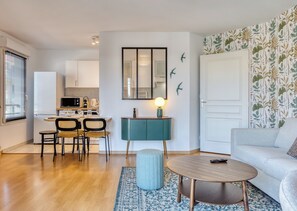 Uma sala de estar moderna com um sofá, uma mesa de centro redonda e um espaço de jantar com cadeiras e uma mesa.