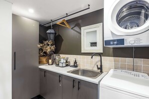 Eine kleine Küche mit Waschmaschine, einer Kleiderstange und einem Waschbecken mit modernem Wasserhahn.