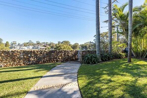 A pathway leading to a stone wall with a residential area in the background. - Lakefront. Terrigal Beach Walk. Sleeps 10 (Wamberal)