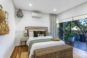 A bedroom with a bed, bedside table, lamp, air conditioning unit, and a view of the outdoors. - Lakefront. Terrigal Beach Walk. Sleeps 10 (Wamberal)
