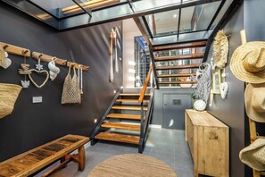 A modern interior with a wooden staircase, a bench, and various woven items displayed on the walls. - Lake House by Coast Hosting (Wamberal)
