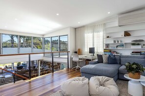 A modern living room with a balcony, a sofa, a desk, and a bookshelf. - Lakefront. Terrigal Beach Walk. Sleeps 10 (Wamberal)