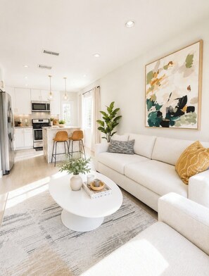 A modern living room with a white sofa, a coffee table, and a painting on the wall. - Stylish California Cottage • Private Backyard • 15 Min to Manhattan Beach & LAX (Redondo Beach)