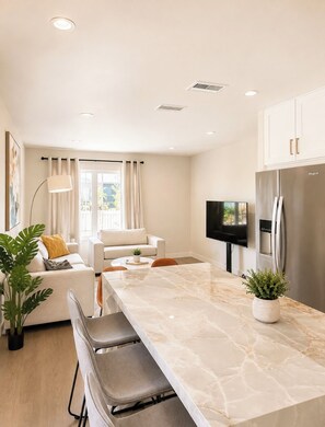 A modern kitchen with a marble countertop, a built-in refrigerator, and a dining area with a sofa and chairs. - Stylish California Cottage • Private Backyard • 15 Min to Manhattan Beach & LAX (Redondo Beach)