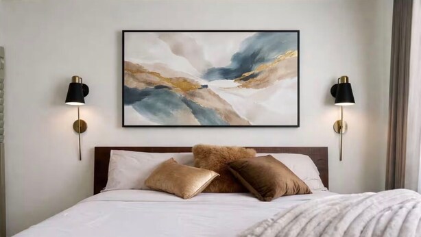 Een slaapkamer met een bed, kussens, een deken en een abstract schilderij aan de muur.