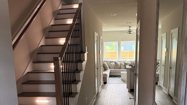 A staircase with wooden steps and black railings, leading to a living area with a sofa and a large mirror. - Houston Hub- Family Getaway, Garage & Yard (Houston)