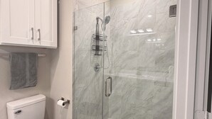 A bathroom with a glass-enclosed shower, a toilet, and a white cabinet. - Houston Hub- Family Getaway, Garage & Yard (Houston)
