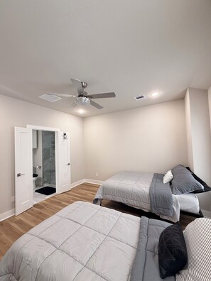 Ein Schlafzimmer mit zwei Betten, einem Deckenventilator, einer Tür zu einem Badezimmer und Holzdielen.