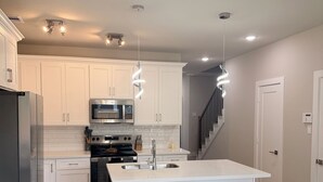 A modern kitchen with white cabinetry, a central island, stainless steel appliances, and pendant lighting. - Houston Hub- Family Getaway, Garage & Yard (Houston)