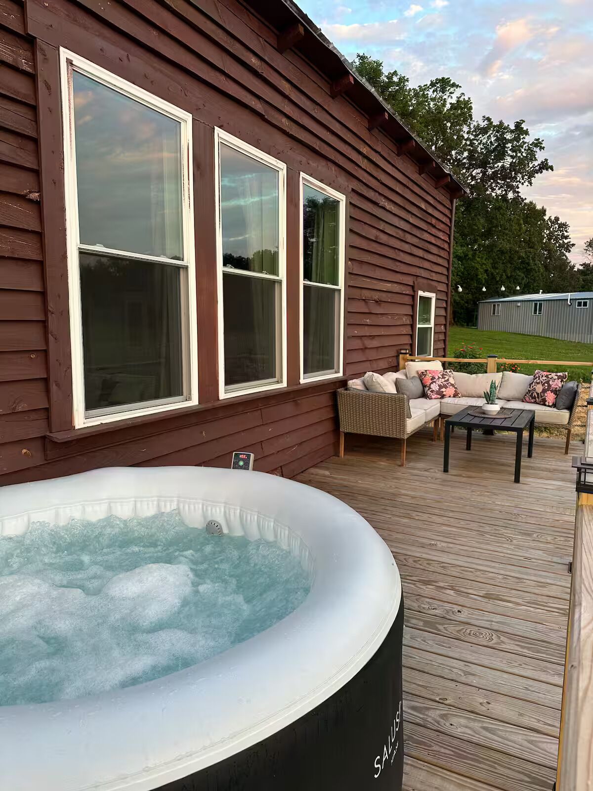 A wooden deck with a hot tub, a sofa, and a table.