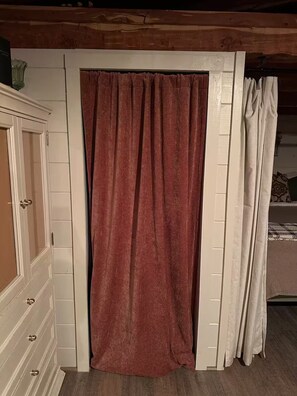 Une pièce avec un plafond en bois, une porte blanche, un rideau rouge et un lit recouvert d’une couvre-lit à motifs.