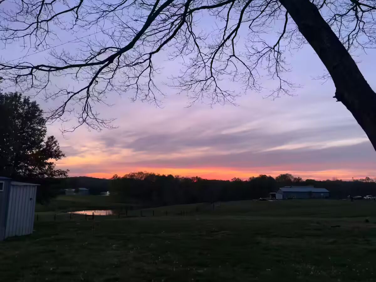 A rural landscape with a clear sky, a body of water, and a farm structure.