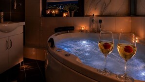 Una vasca idromassaggio con due bicchieri di vino, un asciugamano e vista sulla città illuminata di notte.