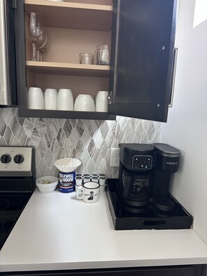 A kitchen with a coffee maker, a bowl of coffee pods, and a cabinet with cups and glasses. - Some Things Just Go Better Together - Nash homes sleep 20! (Nashville)