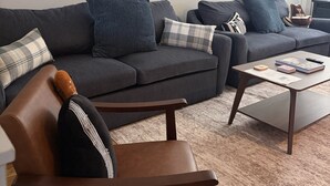 A modern living room with a grey sofa, a brown leather chair, and a coffee table with books and a remote control. - Some Things Just Go Better Together - Nash homes sleep 20! (Nashville)