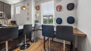 A modern kitchen with a dining area, featuring a wooden countertop, black bar stools, and a wall adorned with hats. - Some Things Just Go Better Together - Nash homes sleep 20! (Nashville)