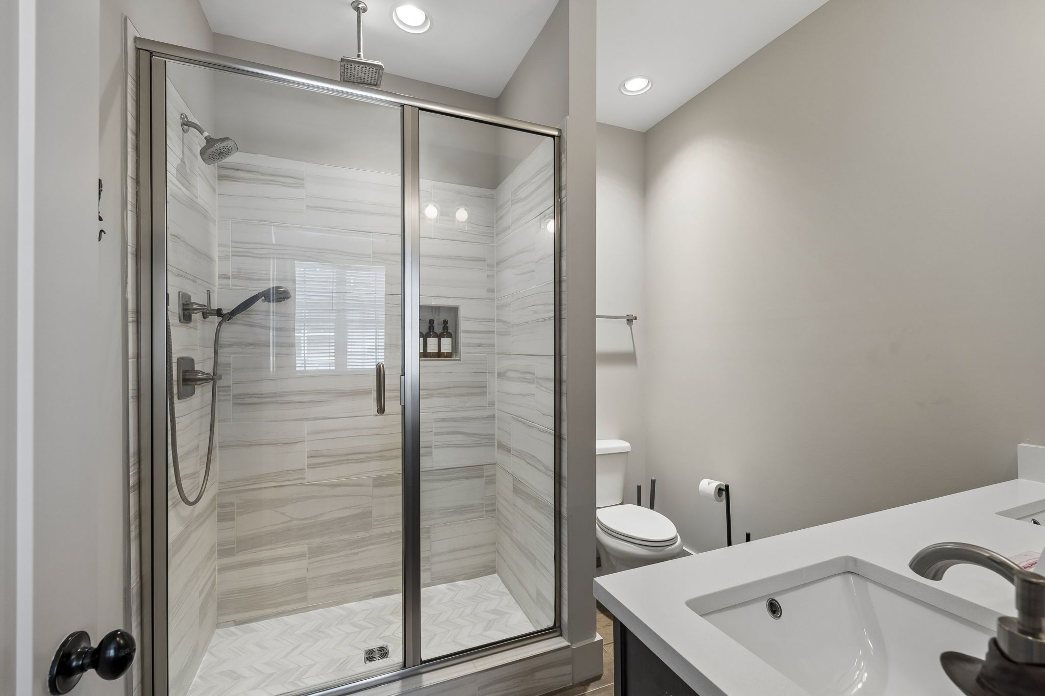 Un baño moderno con ducha envuelta en vidrio, un lavamanos blanco y un inodoro.