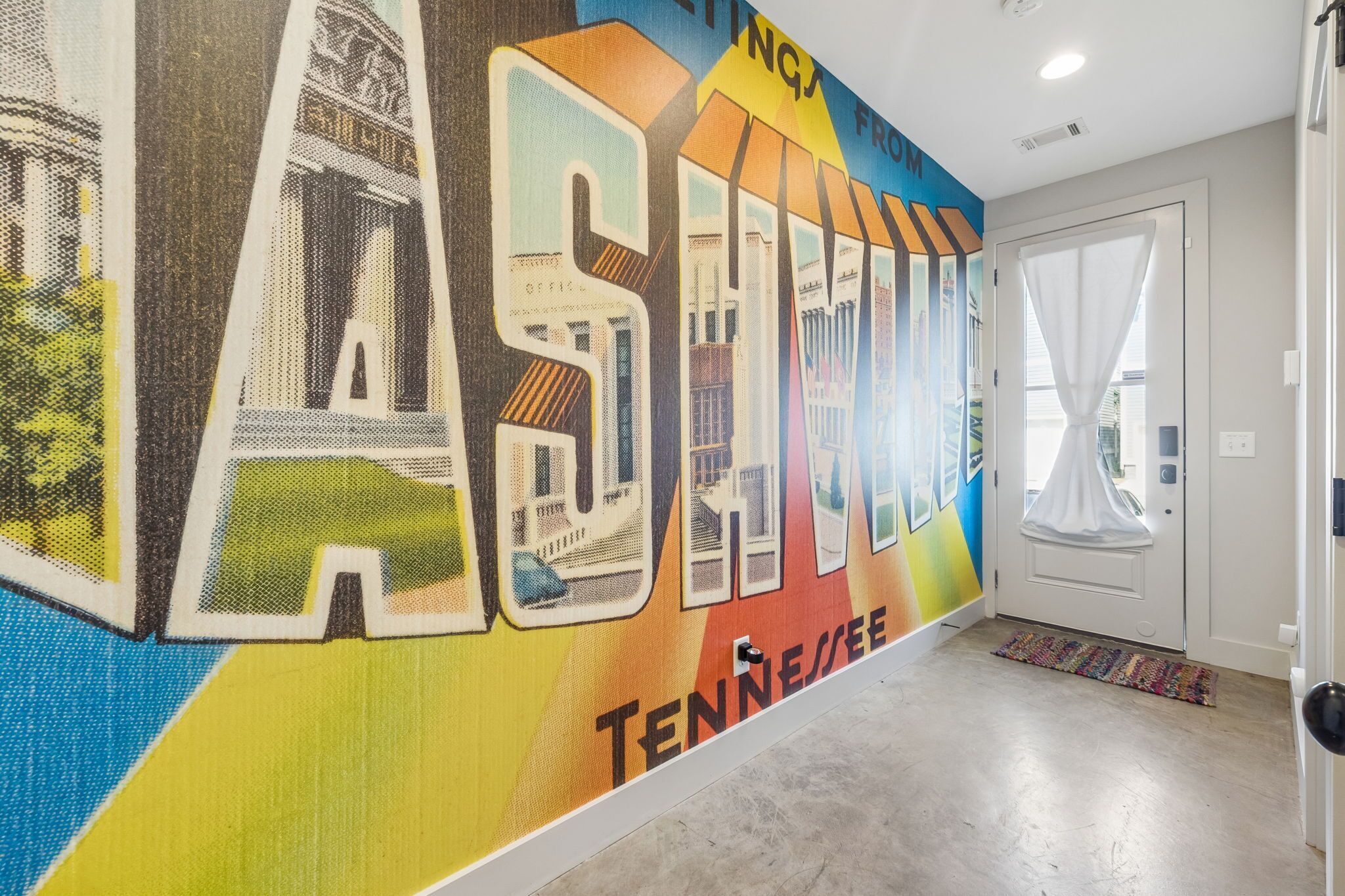 A hallway with a colorful mural on the wall, a door with a window, and a patterned rug on the floor.