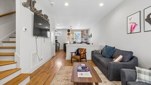 A modern living room with a staircase, a sofa, a coffee table, and a kitchen in the background. - Some Things Just Go Better Together - Nash homes sleep 20! (Nashville)