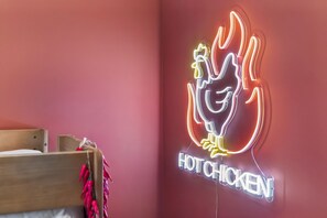 Ein Neon-Schild zeigt ein Hähnchen mit Flammen und den Schriftzug 'HOT CHICKEN' an einer roten Wand.