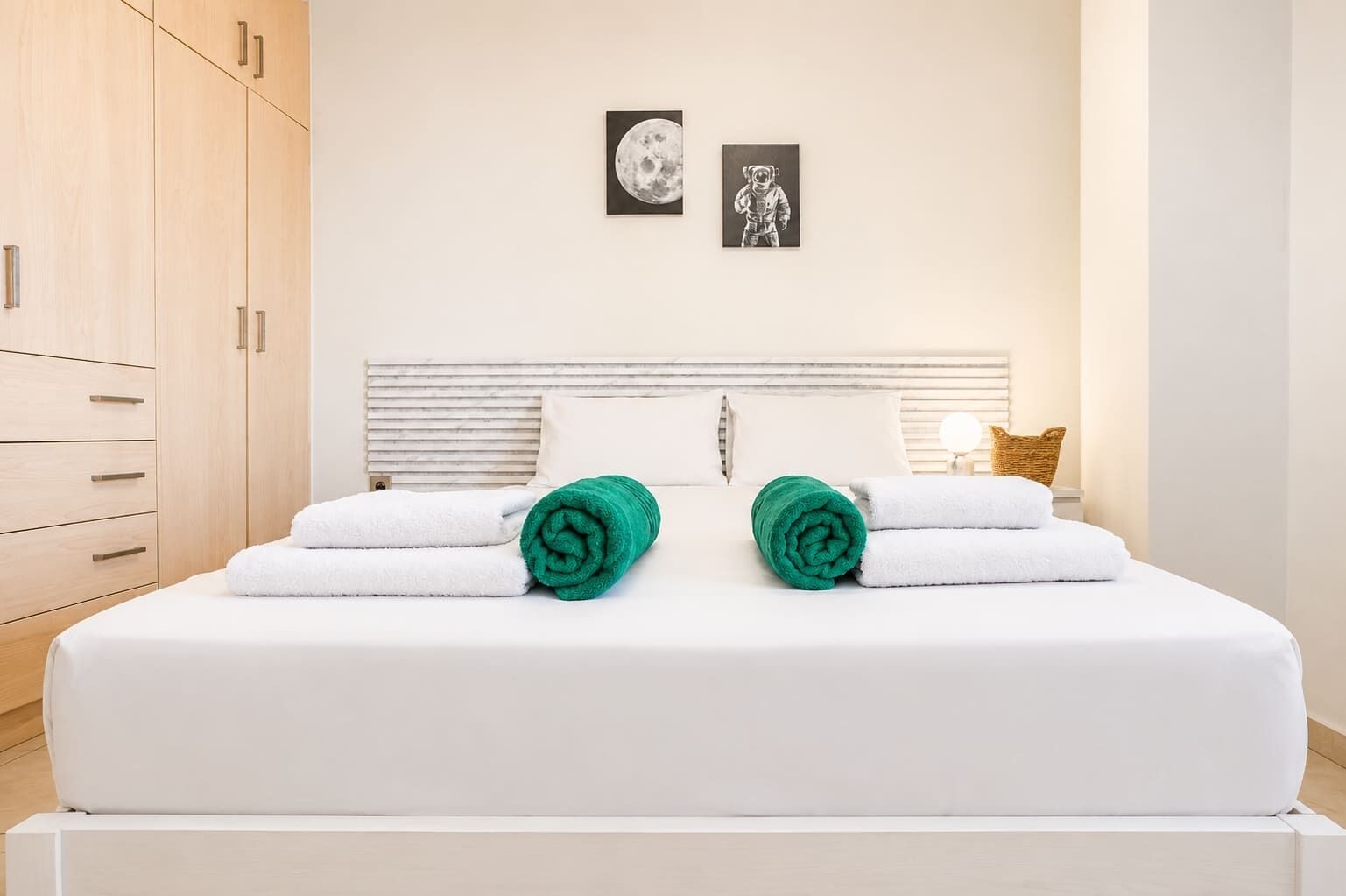 Een hotelkamer met een bed, twee kussens, een nachtkastje, een lamp en kunst aan de muur.