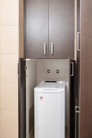 Ein kompakter, moderner Waschraum mit integrierter Waschmaschine und Trockner, Holzschränken darüber und einer gefliesten Wand.