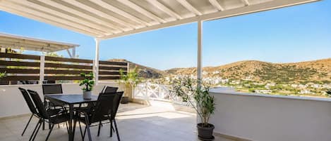 A covered outdoor patio with a table and chairs, potted plants, and a view of a hillside town.