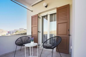 A balcony with two chairs, a small table, and a door with shutters. - Syros Sun Villa - Terrace Open Views near Airport (Manna)