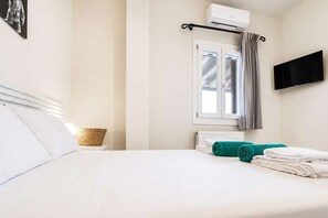 Une chambre d’hôtel avec un lit, une fenêtre avec des rideaux, un appareil de climatisation, un téléviseur à écran plat et un panier en osier posé sur la table de chevet.