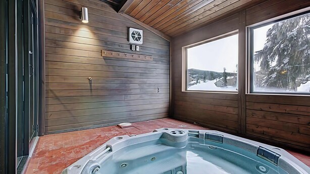 Un interno in legno con una vasca idromassaggio, una finestra con vista innevata e una ventola a muro.