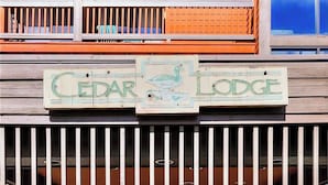 A wooden sign with the text 'CEDAR LODGE' and a bird illustration.