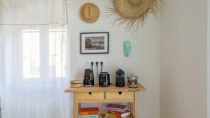 Ein Zimmer mit einem Holztisch, einem Strohhut, einem gerahmten Bild, einer türkisfarbenen Vase und Büchern.