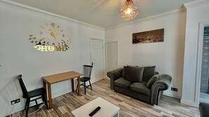 Un salon comprenant un canapé, une table en bois, une chaise, une horloge murale et un luminaire suspendu.