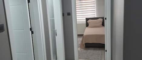 A narrow hallway leading to a bedroom with a bed, a door, and a ceiling light.