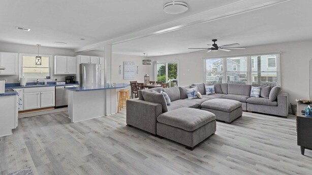 A spacious living area with a grey sectional sofa, a kitchen with white cabinets, and a large window providing natural light. - 1 Block to Beach, 4BR Ship Bottom LBI, Sleeps 8, Walk to All (Ship Bottom)