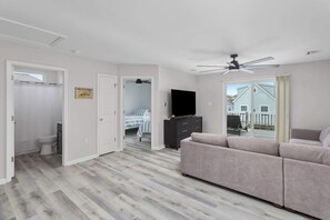 Ein modernes Wohnzimmer mit einem grauen Sofa, einem Flachbildfernseher und einem Deckenventilator.