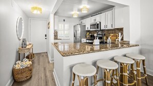 A kitchen with white cabinets, a granite countertop, and a bar area with stools. - Dune Dreams just steps to the beach (Hutchinson Island)