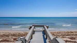 A wooden boardwalk leading to a beach with clear blue water and a sandy shore. - Dune Dreams just steps to the beach (Hutchinson Island)