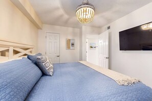 A bedroom with a large bed, a chandelier, a television, and a hallway leading to another room.
