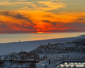 Ein Strand mit Sonnenuntergang, einer Holzpromenade und Liegestühlen.