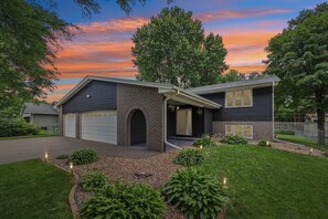Ein zweistöckiges Haus mit Garage, überdachter Veranda und einem gepflegten Vorgarten mit Bepflanzung.