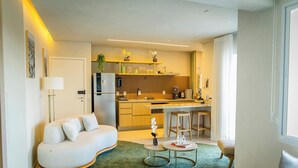 Una sala de estar moderna con sofá, mesa de centro y zona de cocina con refrigerador, estufa y taburetes de bar.